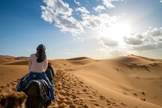 Young girl wearing headscarf riding a dromedary through the erg chebbi Sahara desert in Morocco. High quality photo