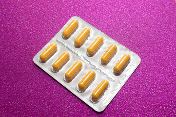 yellow capsules pills pills in a silver blister on a crimson background close-up