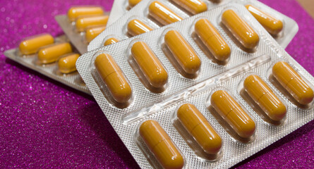 yellow capsules pills pills in a silver blister on a crimson background close-up
