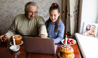 grandfather and granddaughter using laptop on kitchen, online, video call to friends, easter at home during coronavirus covid-19 outbreak.