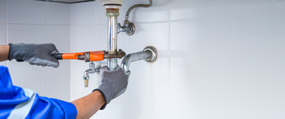 Technician plumber using a wrench to repair a water pipe under the sink. Concept of maintenance, fix water plumbing leaks, replace the kitchen sink drain, cleaning clogged pipes is dirty or rusty.