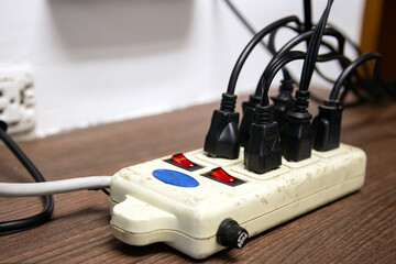 Old and damaged electric adapter power plug has many appliances are plugged outlet socket concept...