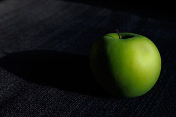Closeup of fresh and juicy organic ripe green apple in black fabric table background with natural side lighting.