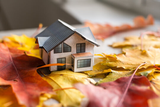 mockup model house and leaves near laptop computer on a table. Autumn season time