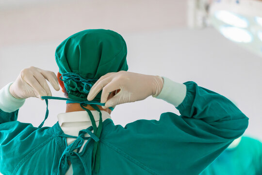 Back view of surgeon tying surgical cap in preparation, Medical team performing surgical operation in operating room, Team surgeon at work in operating room