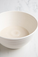 Obraz na płótnie Canvas Nut milk bag squeezing milk into a white bowl with almond milk placed on a white marble surface
