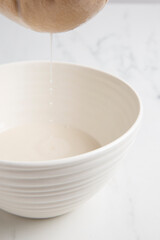 Fototapeta na wymiar Nut milk bag squeezing milk into a white bowl with almond milk placed on a white marble surface