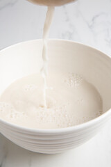 Nut milk bag squeezing milk into a white bowl with almond milk placed on a white marble surface