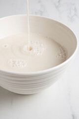 Nut milk bag squeezing milk into a white bowl with almond milk placed on a white marble surface