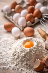 Fototapeta na wymiar Egg yolk on top of a pile of flour with more eggs and egg shells in preparation of dough for pasta or baking