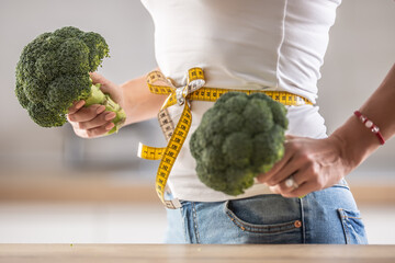 Tape measure tied to a waist of woman holding two broccolis