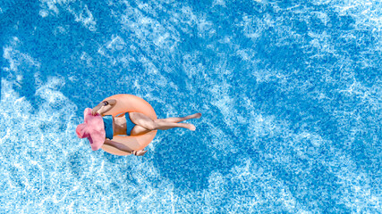 Beautiful woman in hat in swimming pool aerial top view from above, young girl in bikini relaxes and swims on inflatable ring donut and has fun in water on family vacation, tropical holiday resort