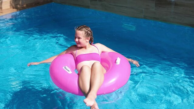 Girl floating on pink inflatable ring in swimming pool. Traveling and vacation concept