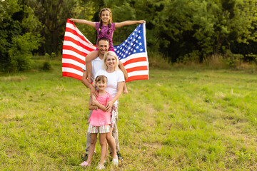 Patriotic holiday. Happy family, mother and daughters with American flag outdoors on sunset. USA...