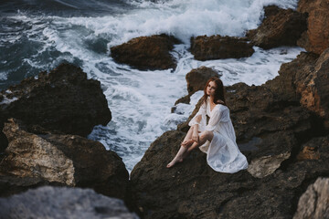 a woman sits on a cliff in a white dress by the ocean cloudy weather unaltered