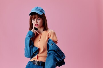 Positive young woman in a cap and denim jacket posing pink background unaltered