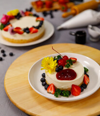 Pouring blueberry sauce onto delicious sweet cheesecake decorated with fresh berry fruits, and flowers on a wooden plate, for a birthday, Valentine day and celebration