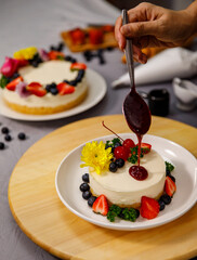Pouring blueberry sauce onto delicious sweet cheesecake decorated with fresh berry fruits, and flowers on a wooden plate, for a birthday, Valentine day and celebration