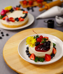 Pouring blueberry sauce onto delicious sweet cheesecake decorated with fresh berry fruits, and flowers on a wooden plate, for a birthday, Valentine day and celebration