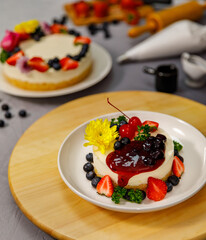 Pouring blueberry sauce onto delicious sweet cheesecake decorated with fresh berry fruits, and flowers on a wooden plate, for a birthday, Valentine day and celebration