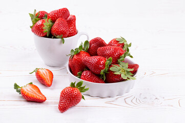 Juicy strawberries berries in a white ceramic bowl and cup on a white shabby wooden table in a rustic style, copy space