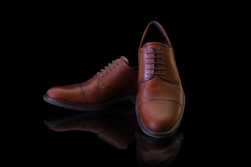 Pair of unbranded brown genuine leather men&rsquo;s shoes on black reflective surface. Product photography and shopping concept