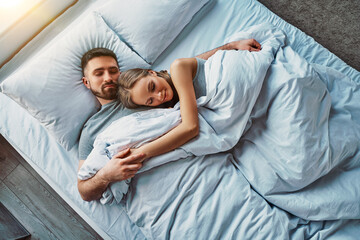 Beautiful young couple sleeping in bed hugging. Calm and healthy sleep. Top view.