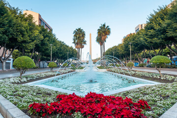 Water fountain and flowers next to the palm trees in the Belen street of the Rambla de Almeria, Andalucia. Spain. Costa del sol in the mediterranean sea - obrazy, fototapety, plakaty