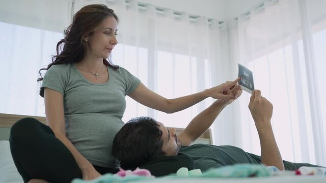 Caucasian Pregnant Couple Looking at Ultrasonographic Image of Baby in Bedroom