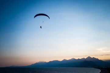 Silhouette of a man on a paraglider flying over the sea at sunset.