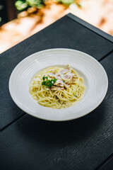 Carbonara in white plate on black wooden table