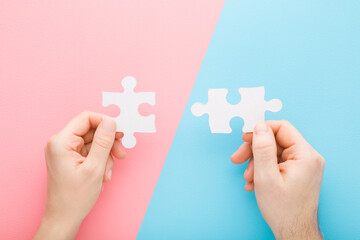 Naklejka premium Young adult man and woman hands holding and putting together white puzzle pieces on light pink blue table background. Pastel color. Closeup. Concept of relationship compatibility. Top down view.