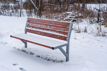 A brown snow-covered bench at the sidewalk.