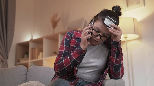 Debt problem. Blocked credit card. Phishing scam. Unhappy woman talking on phone call worried with bank fraud cyber crime on couch at home.
