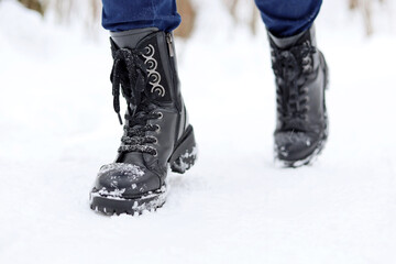 Female legs in black leather lace-up boots on a snow. Woman walking on winter street, warm footwear for cold weather