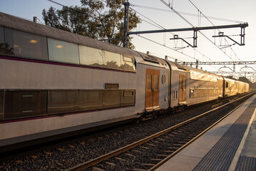 Obraz premium Rail travel. Modern intercity train on a railway platform. Passenger train on the railway in the evening. Railway station Castelldefels. Platform, rails and wires going into perspective.