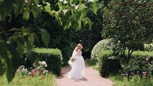 The bride runs through the park among the greenery and smiles cheerfully at the camera. The general plan