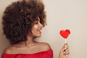 Beautiful portrait of an African girl with a heart shaped lollipop. Valentine's Day. Symbol of love