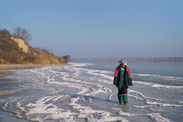 A woman in a colorful thermal costume enjoying winter while walking on a frozen lake with blue sky in the background. Freedom