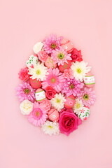 Easter egg shape concept with decorated eggs and flowers on pastel pink background. Spring and Easter abstract design. Top view, copy space.