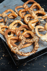 Fresh prepared homemade soft pretzels. Different types of baked bagels with seeds on a black background.