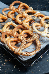 Fresh prepared homemade soft pretzels. Different types of baked bagels with seeds on a black background.