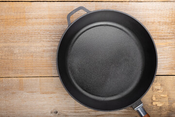 Empty cast iron pan on wooden culinary background, space for text.