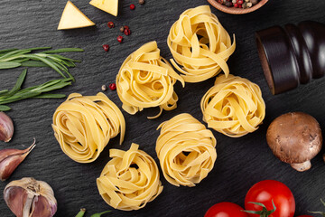 Raw pasta tagliatelle with fresh tomatoes, peppers, mushrooms,asparagus beans, spices and cheese on black table.