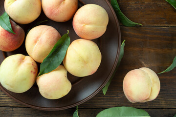 Ripe peaches with leaves in a clay plate on a wooden table.