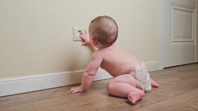 Baby toddler reaches into the electrical outlet on the home wall with his hand. Danger and protection of child fingers from electric shock