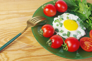 Breakfast of scrambled eggs, tomatoes, parsley on a green plate on a wooden table. 
