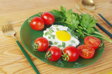 Breakfast of scrambled eggs, tomatoes, parsley on a green plate on a wooden table. 