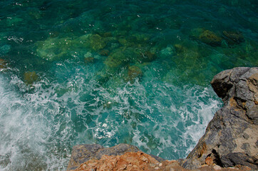 Waves splash against rocks. Marine theme with copy space. Top view natural background of rippled sea-green sea water. Aerial view of aquamarine sea surface. Rough sea and stone texture.