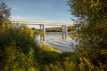 Wild overgrown bank of the Oka River, view of the Puchkovsky Bridge, sunny day in September 2021, Kaluga, Russia